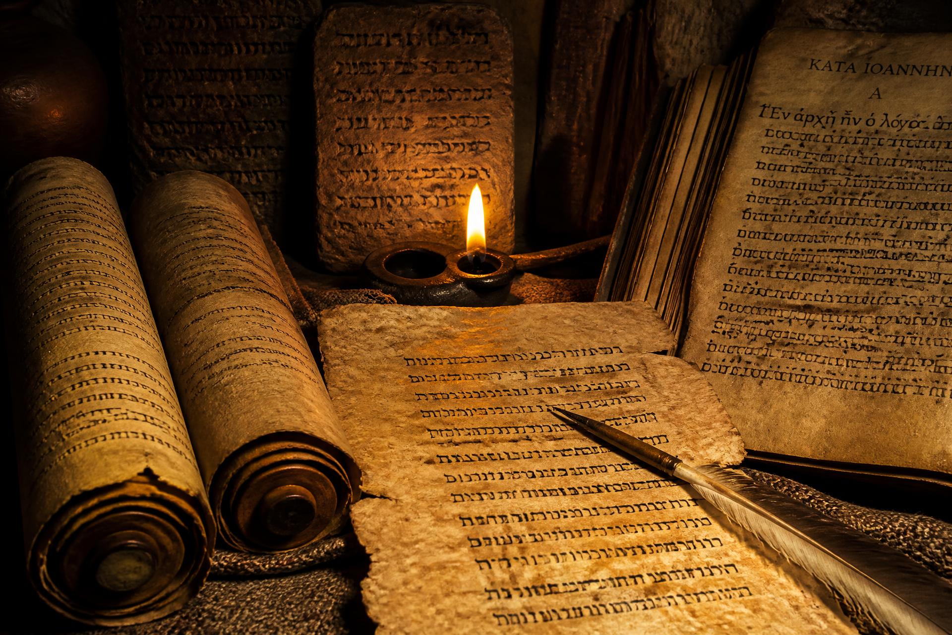 Manuscritos bíblicos antigos em hebraico e grego iluminados por uma vela